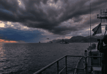 🚨 Trump’s Iran Deadline Arrives: Strikes, Ceasefire Talks, and the World Holding Its Breath Naval officer with binoculars on ship, fleet in distance.